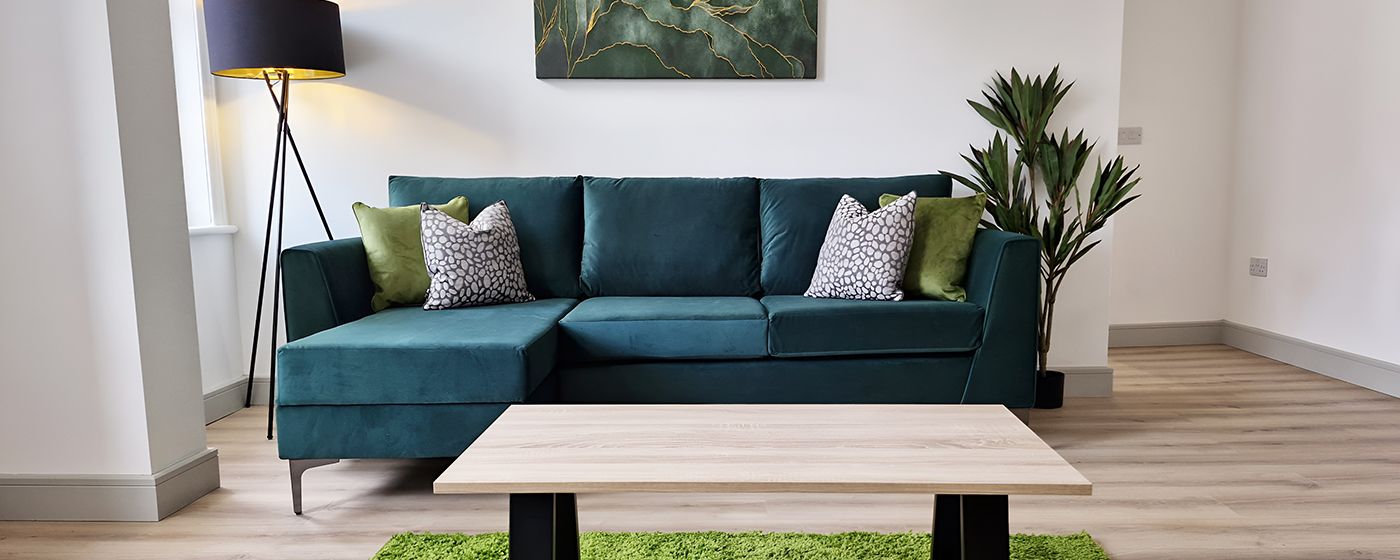 A furnished living room with a teal corner sofa, coffee table and green cushions, supplied by Your Property Furnished